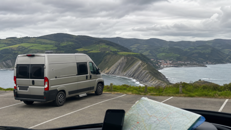 Camper en la costa del País Vasco con acantilados verdes y pueblo marinero